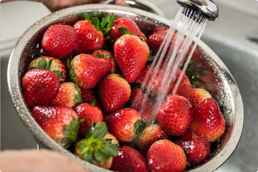 A woman washes strawberries at the sink